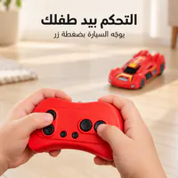 يدان تمسكان جهاز التحكم الأحمر والسيارة أمامهما. التحكم بيد طفلك يوجّه السيارة بضغطة زر